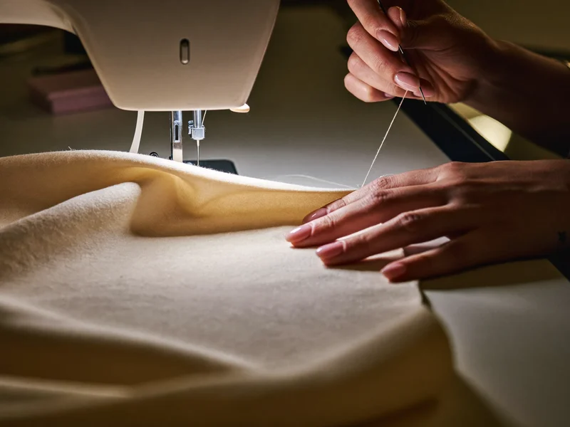 Mâini care coase o cusătură fină pe jerseu moale de bumbac, la masa de croit